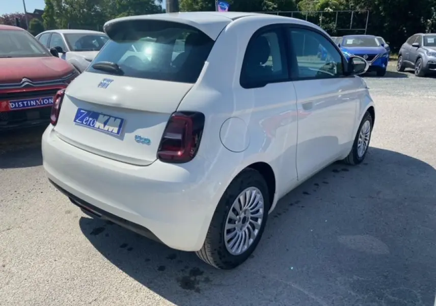 Vue 3/4 arrière droite d'une FIAT 500 électrique blanche métallisée, avec feux arrière foncés et jantes multibranches.