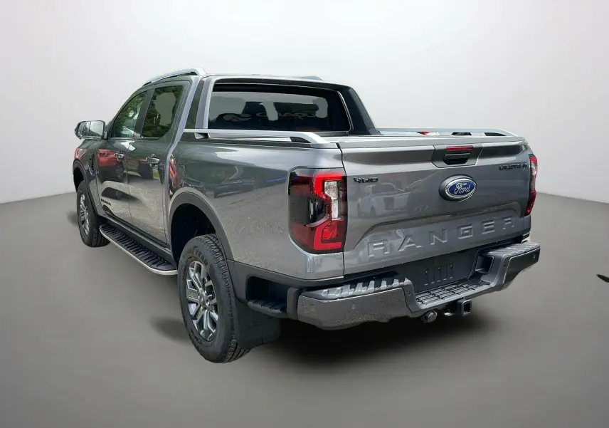 Vue 3/4 arrière droite d'un Ford Ranger gris carbone avec double cabine et barres de toit visibles.