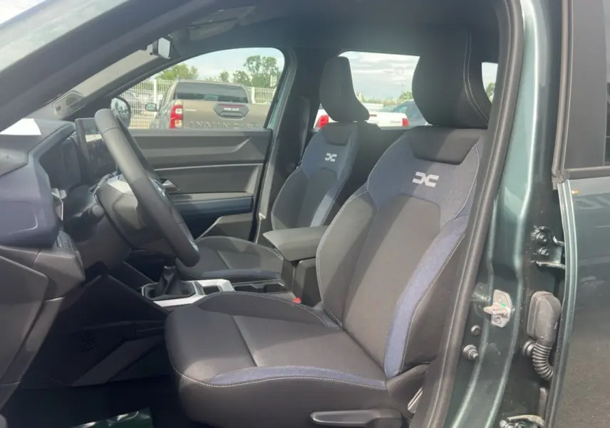 Vue intérieure côté conducteur du Dacia Bigster vert cèdre, montrant les sièges avant avec logo DC et volant soft feel.