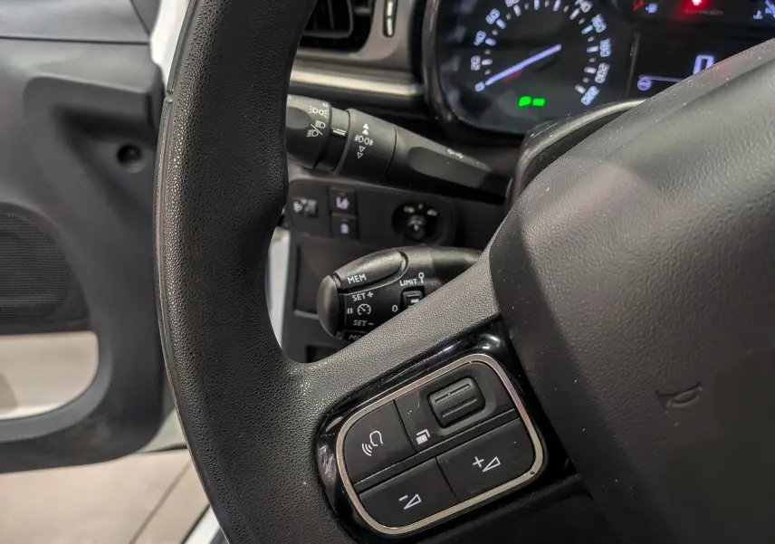 Gros plan sur le volant côté gauche d'une Citroën C3 Société blanc banquise, avec commandes audio intégrées visibles.