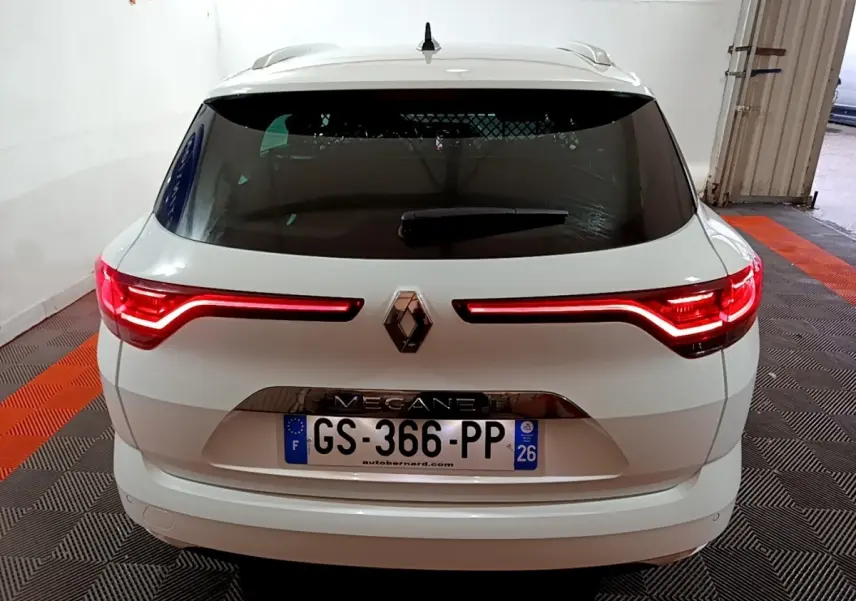 Vue arrière d'une Renault Mégane blanche 2023 avec feux LED allumés dans un garage.