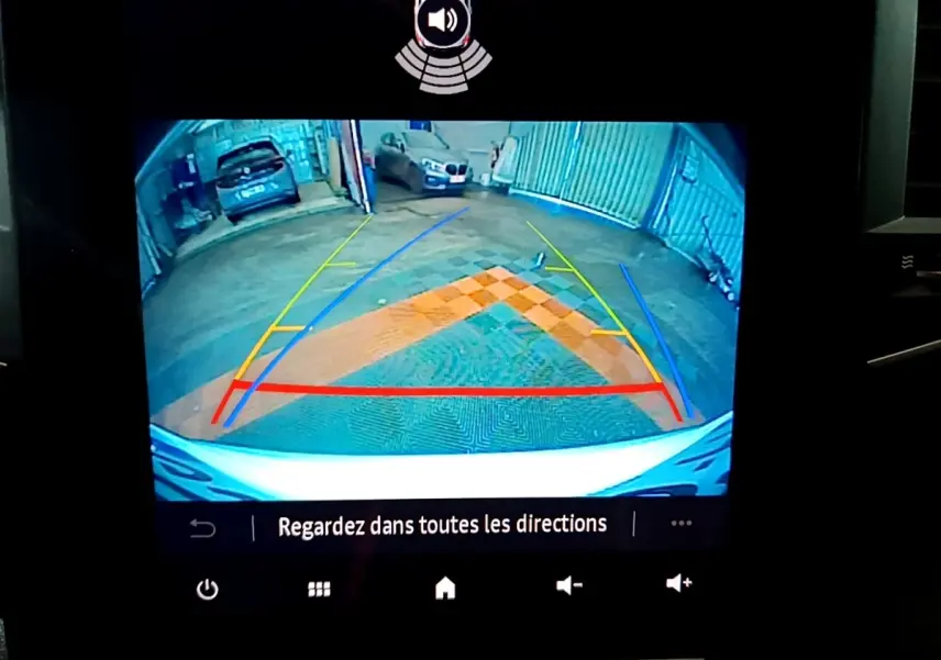 Vue caméra de recul de la Renault Mégane blanche, avec lignes de guidage colorées et vue sur un parking intérieur.