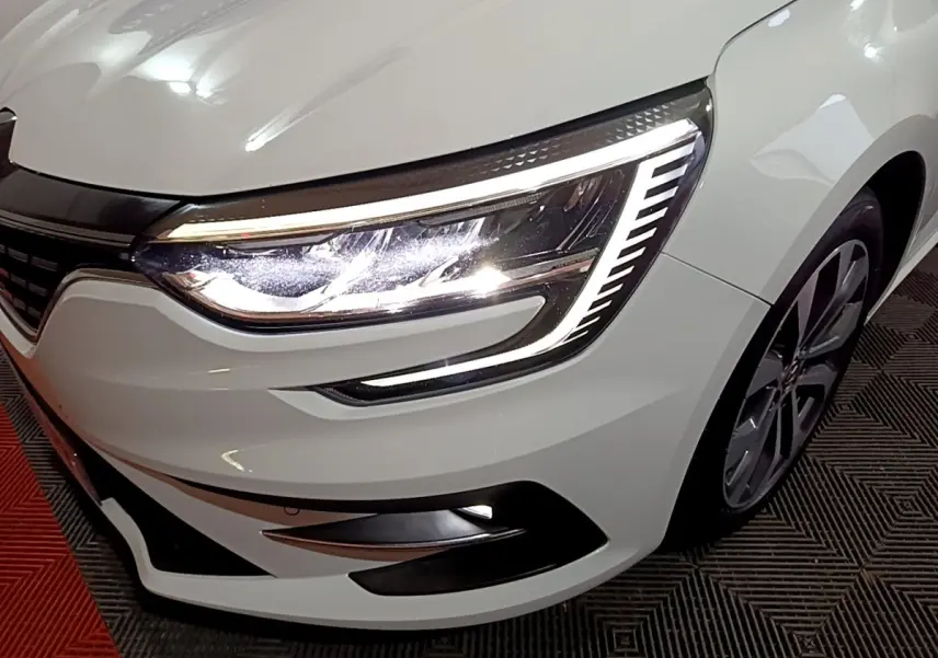Gros plan sur l’avant droit blanc de la Renault Mégane 2023, mettant en valeur son phare LED au design distinctif.