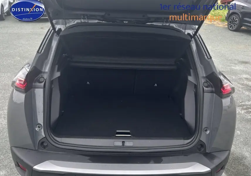 Coffre ouvert à l’arrière d’un Peugeot 2008 gris sélénite, montrant l’espace de chargement vide et les feux arrière LED allumés.