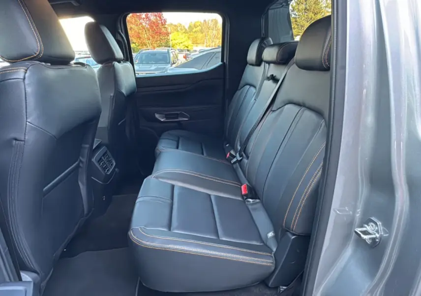 Vue intérieure arrière côté droit du Ford Ranger PHEV 281 Wildtrak gris iconic avec sièges cuir noirs et surpiqûres orange.
