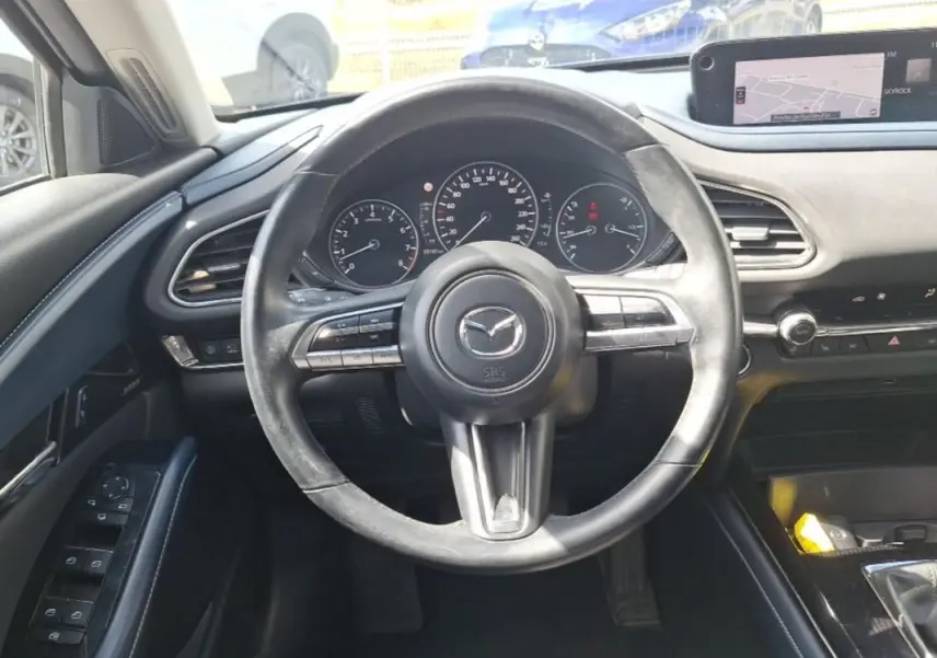 Vue intérieure centrée sur le volant noir multifonctions et le tableau de bord avec écran GPS du Mazda CX-30 gris 2020.