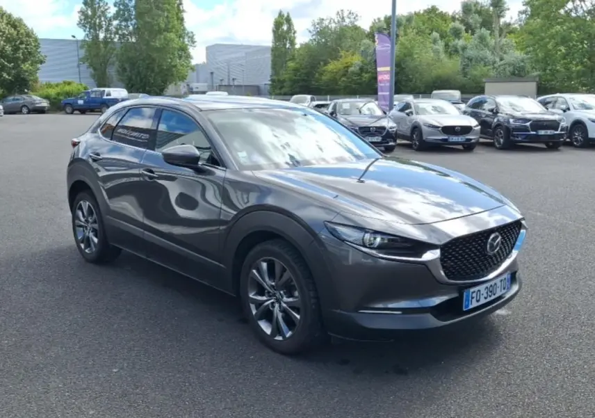 Vue 3/4 avant d'un Mazda CX-30 gris métallisé avec jantes aluminium, vitres surteintées et calandre noire ajourée.