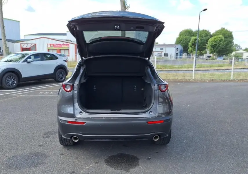 Vue arrière d'un Mazda CX-30 gris 2020 avec coffre ouvert, feux ronds et double sortie d'échappement visibles.
