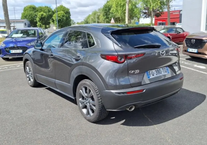 Vue 3/4 arrière droite d'un Mazda CX-30 gris avec vitres surteintées et jantes aluminium sur parking extérieur.