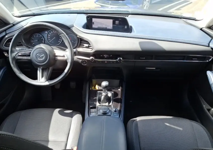 Vue intérieure avant du Mazda CX-30 2020, tableau de bord noir avec écran GPS et levier de vitesse manuel.