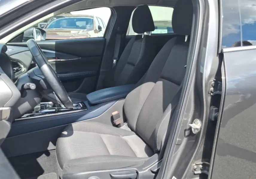 Intérieur avant droit du Mazda CX-30 gris 2020, sièges tissu noirs avec accoudoir central et volant multifonctions.