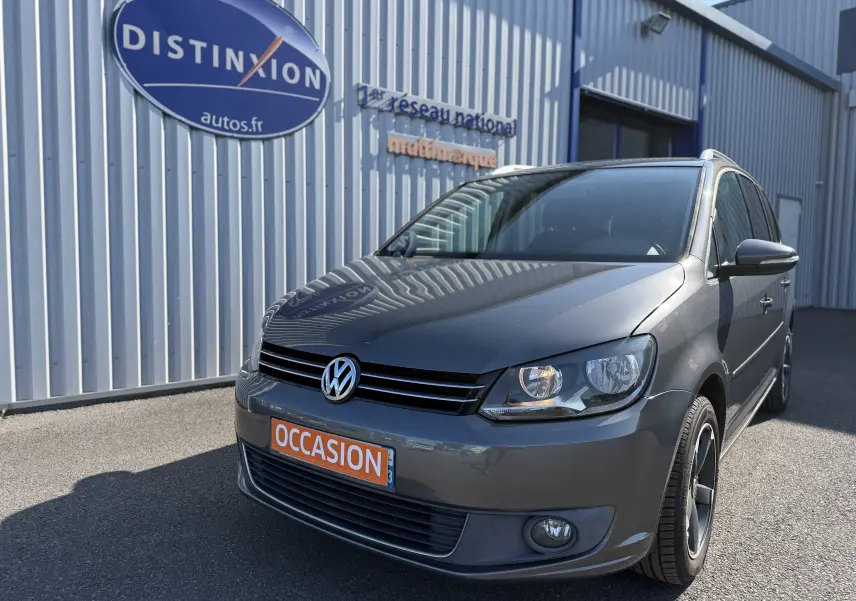 Volkswagen Touran gris 2012 en 3/4 avant droit, avec plaques occasion et jantes alliage noires.