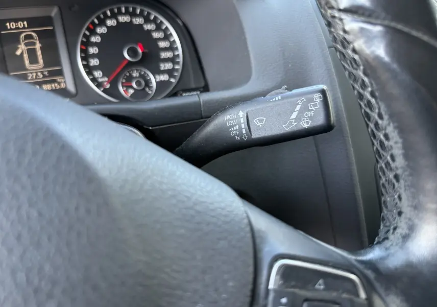 Vue rapprochée du commodo d’essuie-glace à droite du volant noir dans le tableau de bord d’un Volkswagen Touran gris 2012.