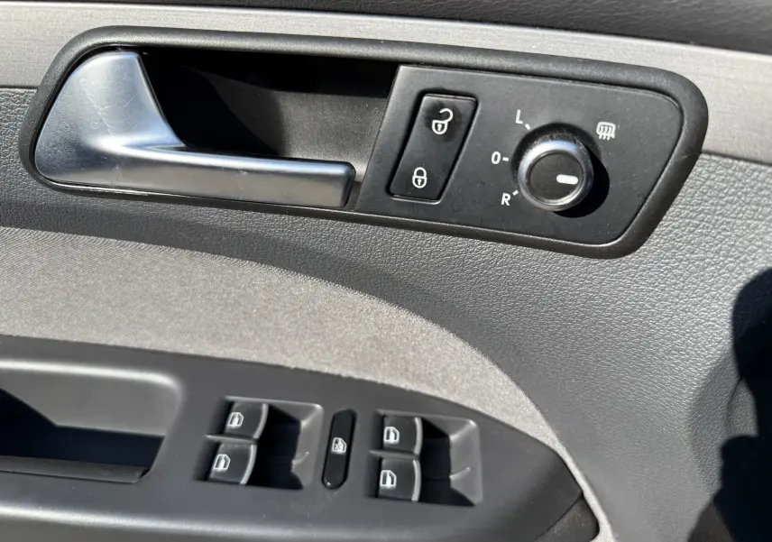 Gros plan sur la commande intérieure côté conducteur du Volkswagen Touran gris, avec poignée, réglage des rétroviseurs et boutons de vitres.