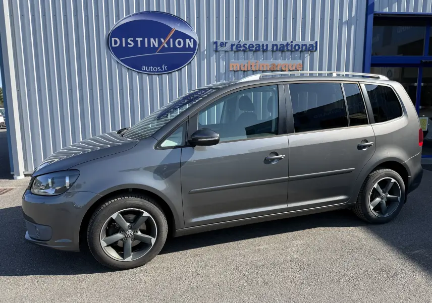 Vue de profil côté gauche d’un Volkswagen Touran gris 2012 avec jantes alliage noires et toit ouvrant visible.