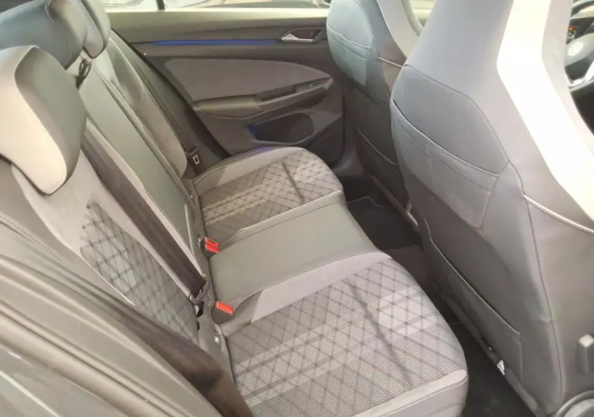 Vue intérieure arrière côté gauche de la Volkswagen Golf 2024 avec sellerie tissu gris à motifs et appuis-tête intégrés.