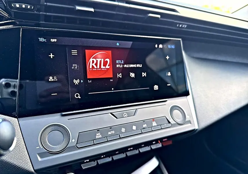Vue rapprochée de la console centrale du Peugeot 308 2025, écran tactile affichant la radio RTL2 et commandes climatisation.