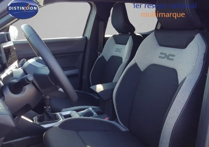 Vue intérieure côté conducteur du Dacia Duster TCE MHEV 140ch Journey 2026, sièges bi-ton noir et gris avec logo DC.