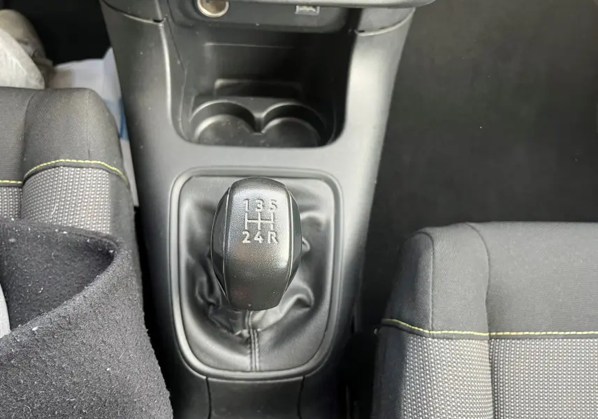 Le levier de vitesses manuel noir vu de dessus dans l'habitacle d'une Citroën C3 blanche de 2019, avec sièges gris et surpiqûres jaunes.