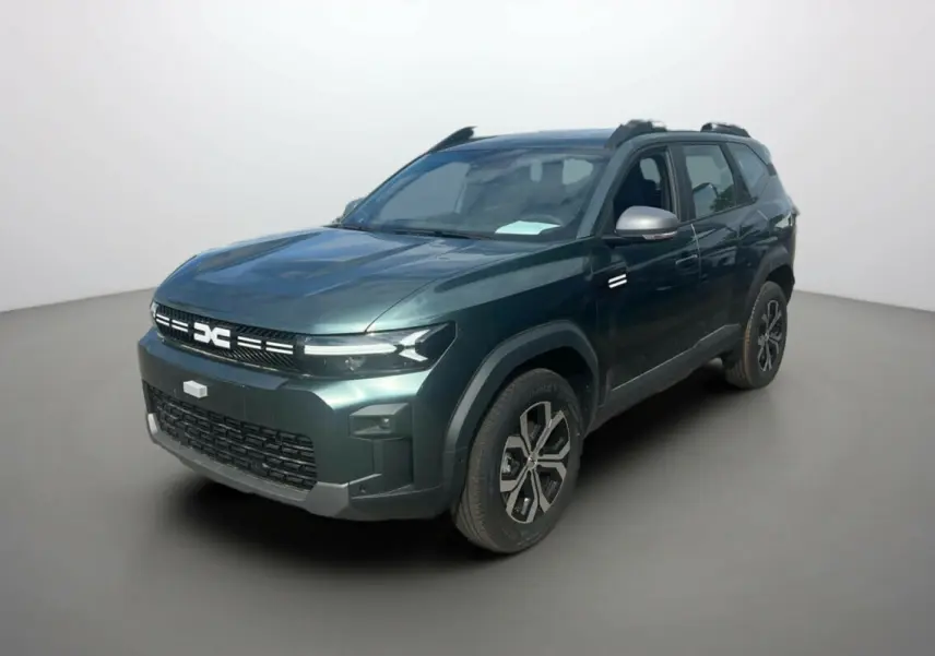 SUV Dacia Bigster vert cèdre en 3/4 avant droit avec barres de toit et jantes alu 17 pouces visibles.