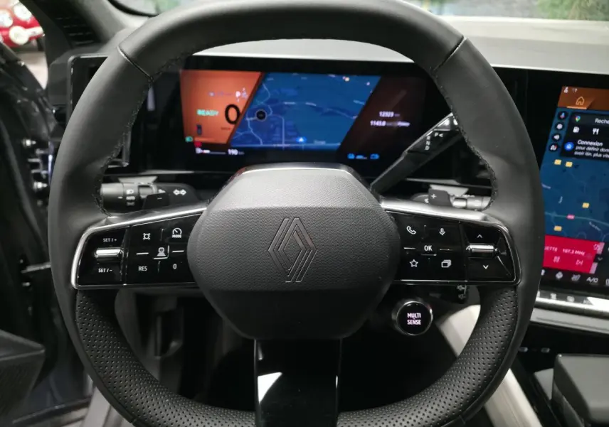 Volant noir perforé de Renault Espace 2025 avec commandes intégrées et écrans numériques en arrière-plan.