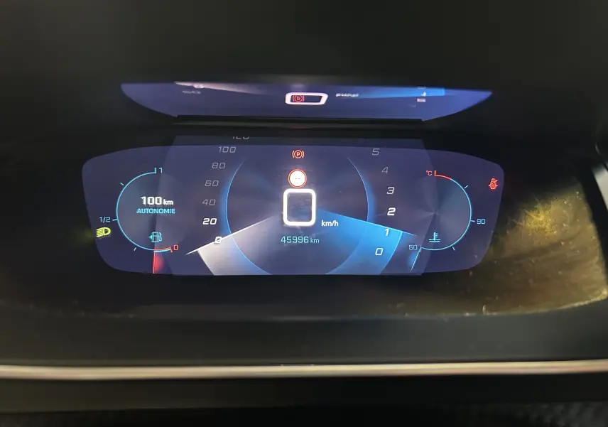 Tableau de bord numérique de Peugeot 208 gris, affichant la vitesse à 0 km/h et l'autonomie à 100 km.