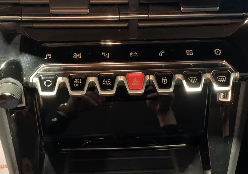 Gros plan sur la rangée de boutons de commande du tableau de bord noir brillant de la Peugeot 208 gris, version PureTech 100 Allure Business.