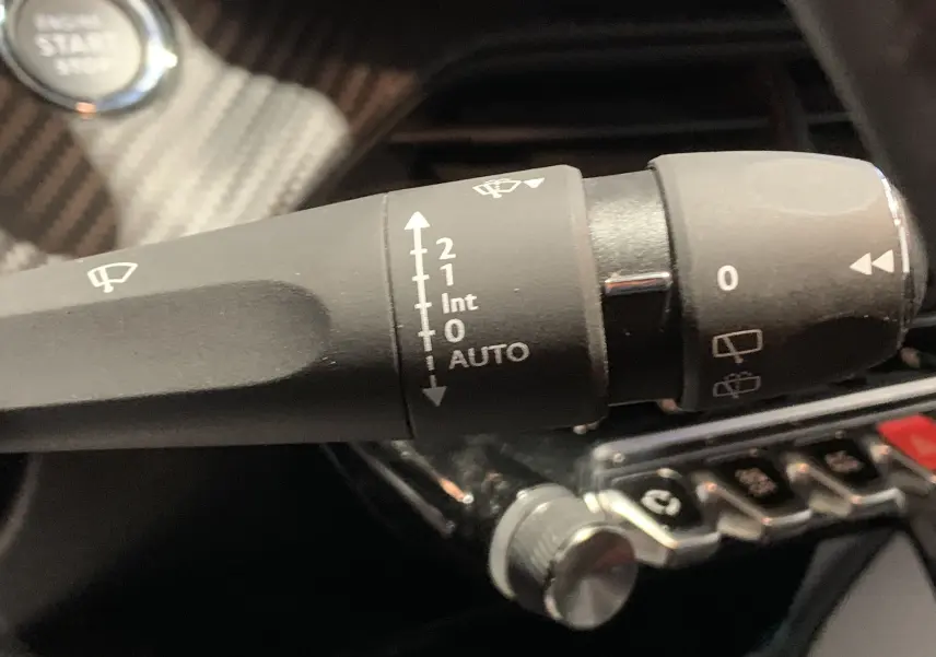 Gros plan sur la manette d’essuie-glace noire dans l’habitacle gris foncé de la Peugeot 208 PureTech 100 Allure Business.