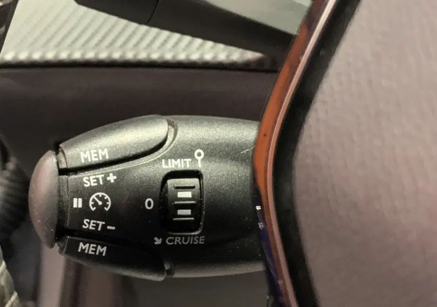 Gros plan sur la commande de régulateur de vitesse à gauche du volant d’une Peugeot 208 gris 2021.