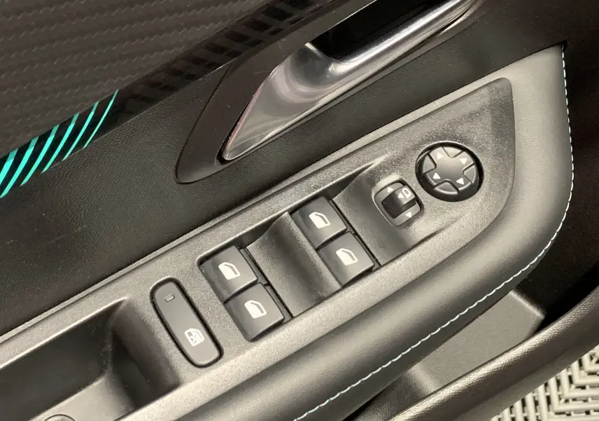 Gros plan sur la commande des vitres électriques côté conducteur de la Peugeot 208 gris, avec surpiqûres blanches et poignée métallique.