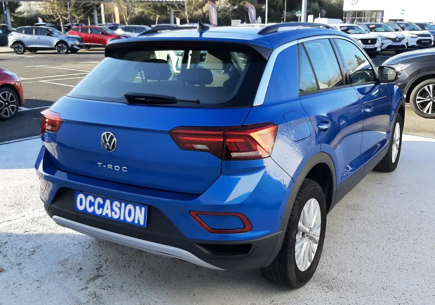 Vue 3/4 arrière droite d'un Volkswagen T-Roc bleu 2022 avec feux LED et toit noir sur parking.