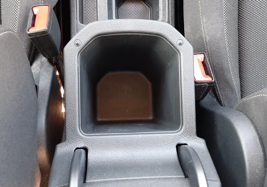 Vue plongeante sur le rangement central noir entre les sièges avant du Volkswagen T-Roc bleu 2022, avec ceintures de sécurité visibles.