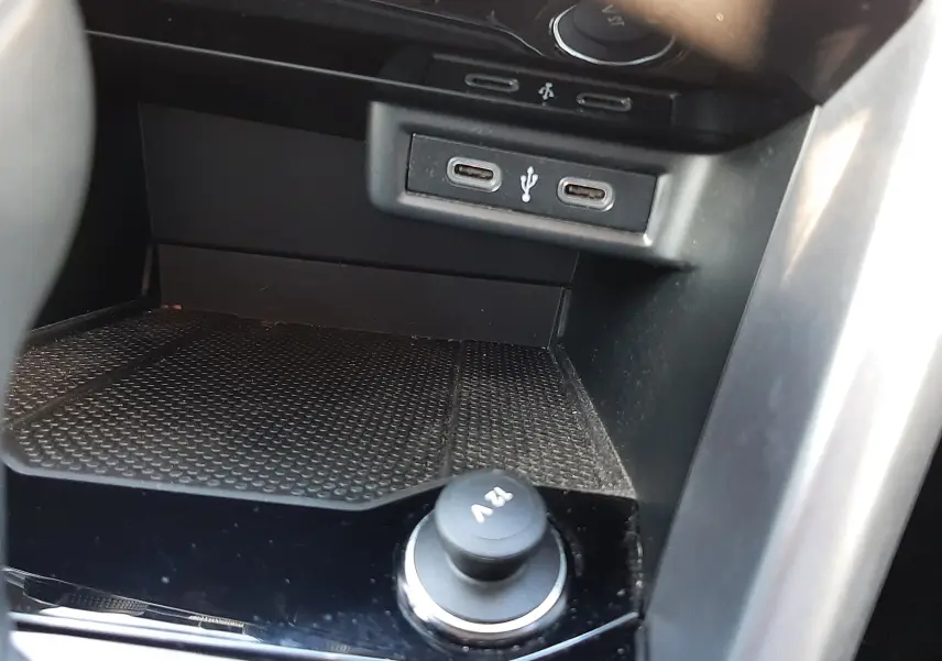 Vue rapprochée de la console centrale du Volkswagen T-Roc 2022, montrant prises USB et prise 12V sur fond noir brillant.