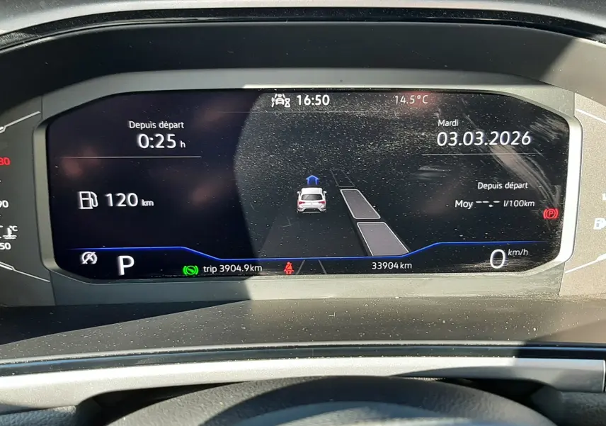 Vue rapprochée du tableau de bord numérique du Volkswagen T-Roc bleu, affichant la date, la vitesse et l'autonomie.