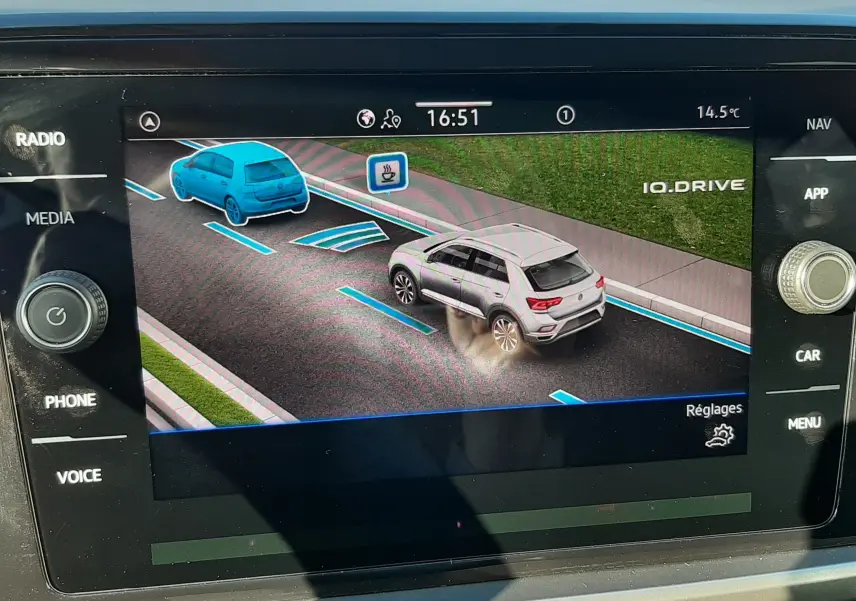 Écran de navigation montrant un Volkswagen T-Roc bleu en stationnement, vue arrière droite avec aides au stationnement activées.