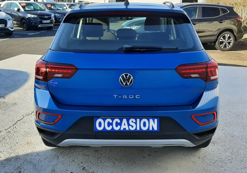 Vue arrière d'un Volkswagen T-Roc bleu 2022 avec plaque "OCCASION" sur un parking extérieur.