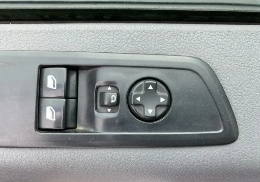 Gros plan sur les commandes électriques des vitres et des rétroviseurs sur la porte intérieure d’un Citroën Jumpy blanc.