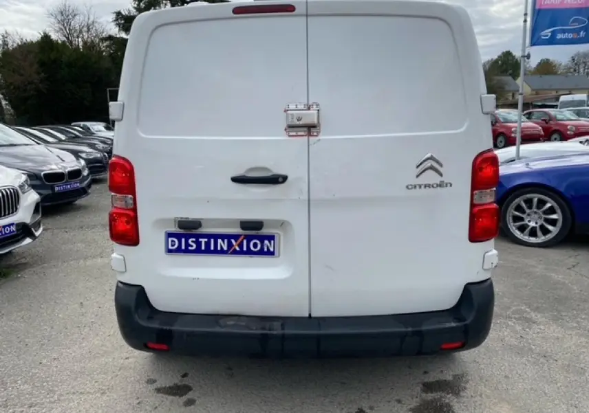 Vue arrière d'un utilitaire Citroën Jumpy blanc avec portes battantes et pare-chocs noir, stationné en extérieur.