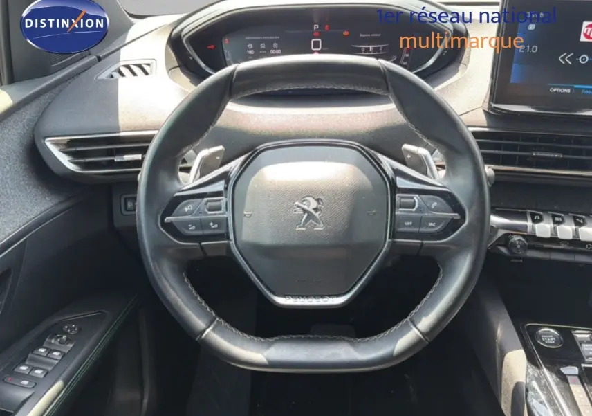 Vue intérieure centrée sur le volant cuir noir du Peugeot 5008 2023 avec tableau de bord digital et commandes intégrées.