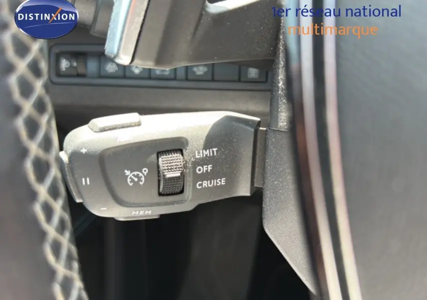 Gros plan sur la commande de régulateur de vitesse à gauche du volant dans un Peugeot 5008 gris Platinium 2023.