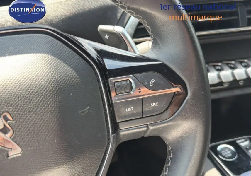Gros plan sur le volant en cuir noir du Peugeot 5008 2023, avec commandes intégrées et palettes au volant visibles.