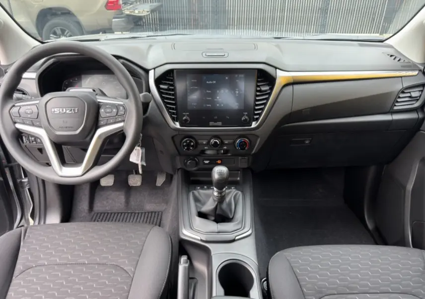 Vue intérieure avant de l'Isuzu D-MAX 2026, tableau de bord noir avec écran tactile et levier de vitesses manuel.