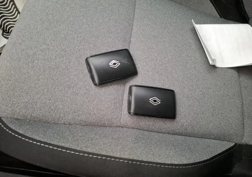 Gros plan sur deux clés noires Renault posées sur un siège tissu gris à coutures blanches, intérieur voiture visible.