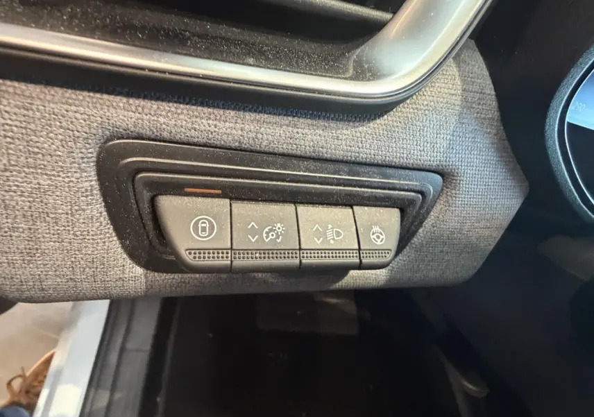 Gros plan sur les commandes d’éclairage et de verrouillage sur la planche de bord tissu gris de la Renault Clio blanche.