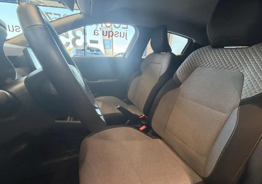 Intérieur de la Renault Clio 2024 vu côté droit, sièges tissu gris avec motifs 3D et volant multifonction noir.