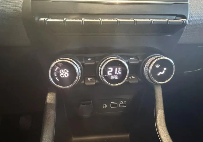 Gros plan sur les commandes de climatisation noires de la Renault Clio blanche, avec affichage digital à 21,5°C.