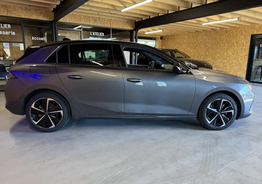 Vue latérale droite d'une Opel Astra gris foncé avec jantes alliage noires et toit noir dans un garage.