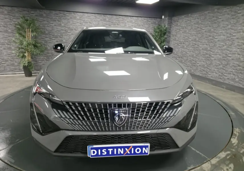 Vue frontale d'une Peugeot 408 gris métallisé avec calandre verticale et logo lion central, en showroom.