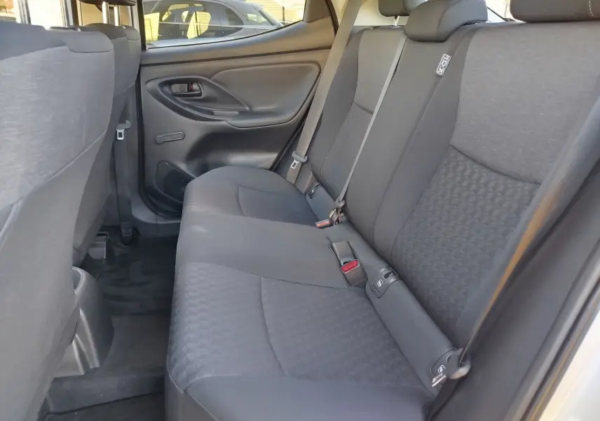 Vue intérieure côté droit des sièges arrière gris tissu de la Toyota Yaris 2023 blanche, avec ceinture et porte arrière visible.
