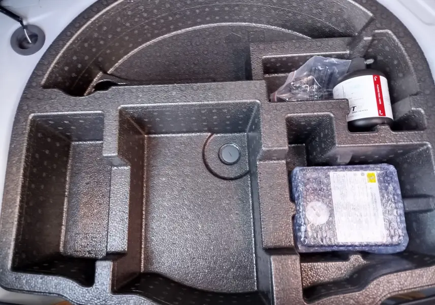 Gros plan sur le rangement en mousse dans le coffre de la Toyota Yaris blanche, avec kit de réparation pneus visible.